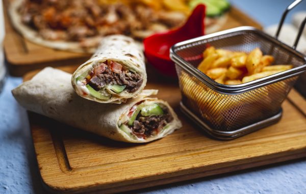 side view doner with meat cucumber tomato sauce and french fries on a board